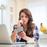 Young nervous woman looking at smartphone and biting her fingernails at home.
